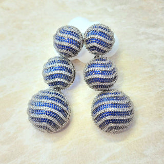Pair of blue and silver striped earrings on a textured beige surface