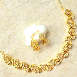 Gold diamond necklace and earrings on a beige surface