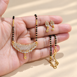 Charlotte white stone black bead gold finish mangalsutra necklace with matching earrings held in hand