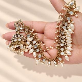 Close-up of Adeline white mirror baahubali jhumka earrings and pearl beaded ear chains held in hand