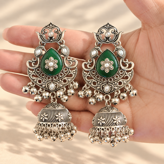 Cressida green oxidised silver kundan style jhumka earrings with dark green teardrop centres and silver bell drops held in hand