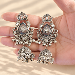 Cressida grey German silver oxidised silver jhumka earrings with floral details and bell drops shown in hand