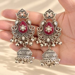 Cressida dark red oxidised silver kundan style jhumka earrings with maroon teardrop centre and silver bell drops held in hand
